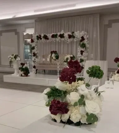 Arche florale blanche et bouquet de roses bordeaux au pied de la scène