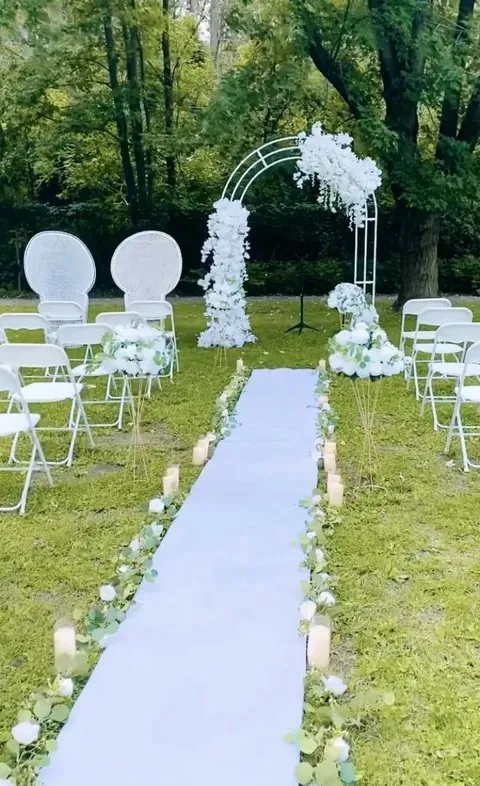 Cérémonie extérieure : allée blanche bordée de bougies et de verdure, arche florale blanche