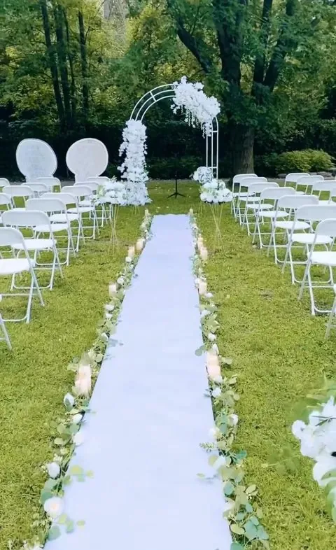 Cérémonie extérieure dans un parc : allée blanche, chaises pliantes et arche florale