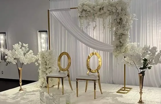 Chaises dorées sous un cadre doré drapé et fleuri de blanc