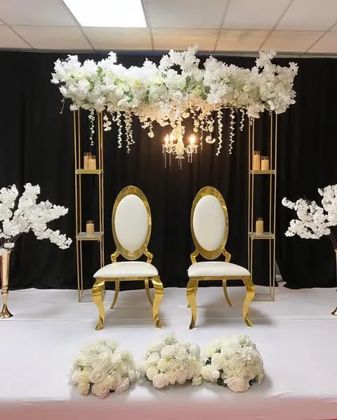 Chaises dorées sous une canopée florale suspendue, fond de rideaux noirs