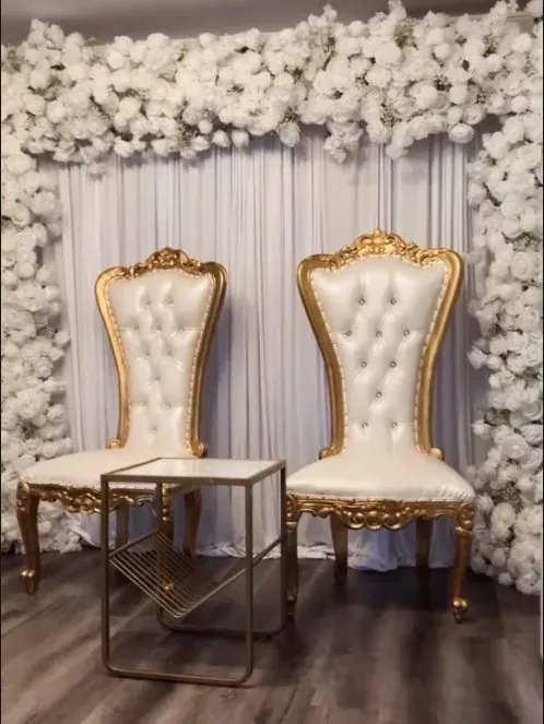 Deux fauteuils trônes dorés devant un mur de roses blanches