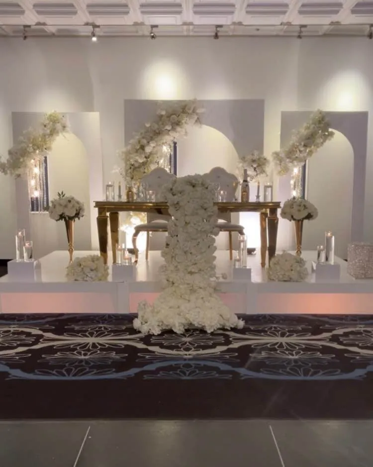Scène de mariage avec panneaux arqués blancs, table d’honneur dorée et cascade de roses blanches
