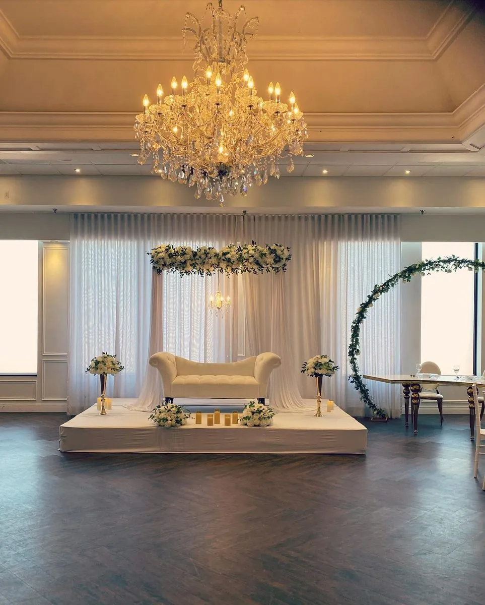 Sofa capitonné sous une guirlande florale suspendue, voilages et lustre en cristal