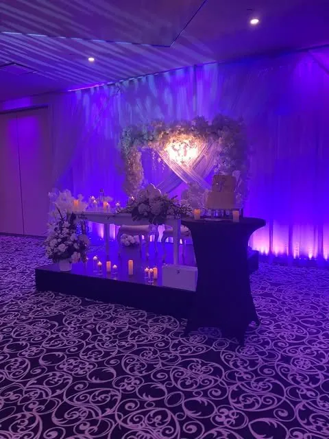 Table d’honneur et gâteau sous éclairage mauve, drapé croisé et fleurs blanches