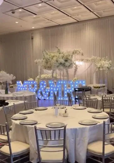 Tables rondes aux centres de table hauts devant des lettres lumineuses MR & MRS